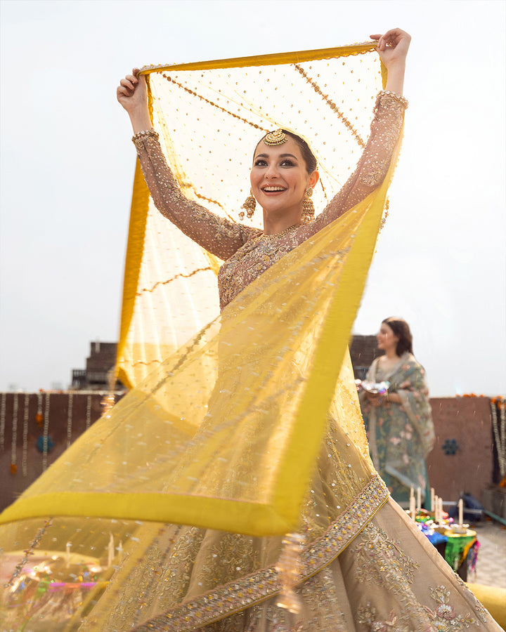 Hand-decorated Mehendi Bridal in golden, tea pink, and yellow hues. includes a handcrafted tissue lehenga, a net dupatta, and a chiffon choli. It has finely embroidered Tropes and Vines made with dabka, marori, and tilla among other crafts. Handcrafted with conscientious care, solid craftsmanship, and a tonne of warmth and affection. 720 by 900 pixels